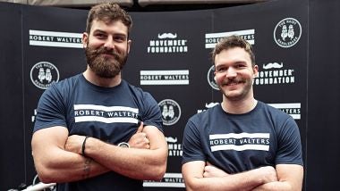 The Hairy Handlebars, Ben Cook and George Cullen, stand side by side with crossed arms at the London launch event at Robert Walters HQ