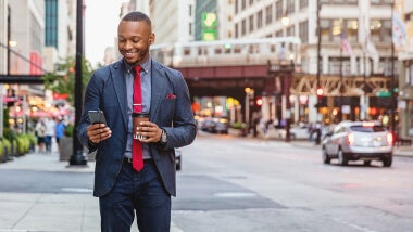 Man wearing suit walking in city and smiling at his mobile phone