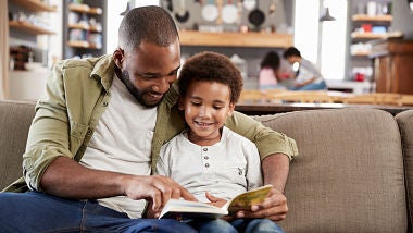 Father and son reading together on sofa at home